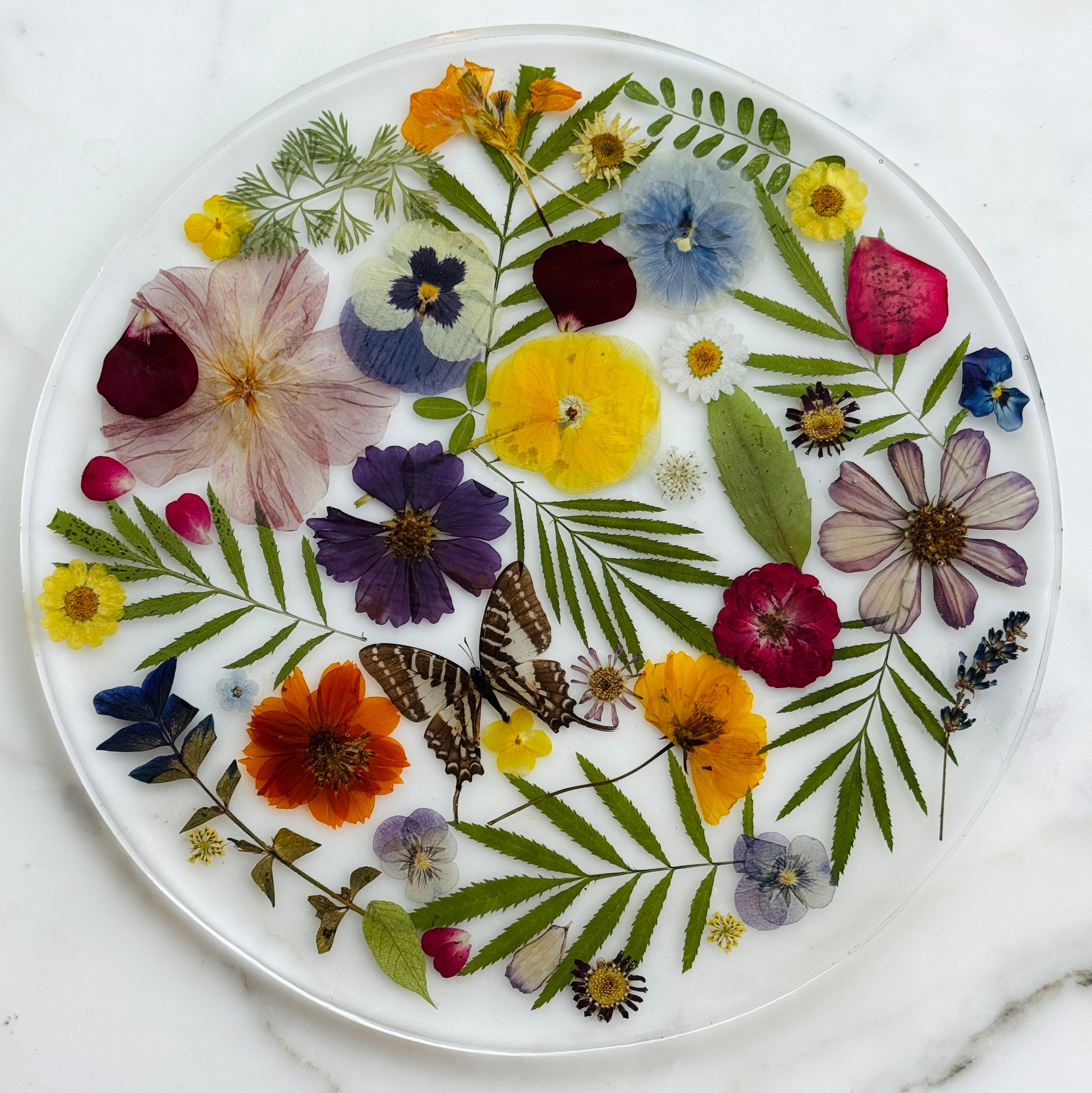 Decorative plate with pressed flowers and butterflies on a marble surface
