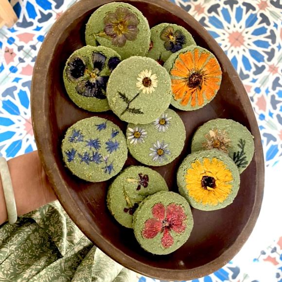 A dozen gluten free matcha flower pressed shortbread cookies on a brown plate with various floral designs.